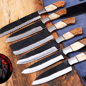 May include: Set of six black chef knives with wooden and bone handles. The knives are arranged in a row on a blue and brown surface. The knives are all different sizes and have a black blade with a polished finish. The handles are made of wood and bone and have a natural finish. The knives are labeled "Sultan Knife Collection".