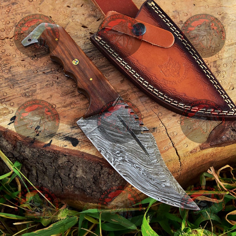 May include: A Damascus steel knife with a wooden handle and a leather sheath. The knife has a unique pattern on the blade and a serrated edge.