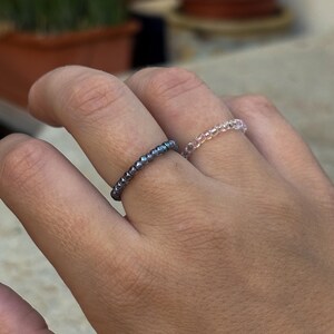 Könnte beinhalten: Zwei Perlenringe an einem Finger. Ein Ring besteht aus dunkelgrauen Perlen und der andere aus klaren Perlen.