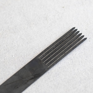 Puede incluir: Primer plano de una aguja de tatuaje negra con múltiples puntas. La aguja es afilada y puntiaguda, y está diseñada para usarse en una máquina de tatuaje.