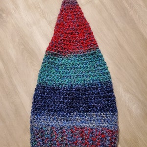 Op de afbeelding: Een driehoekige gehaakte muts met strepen van rood, turquoise, blauw en paars garen.