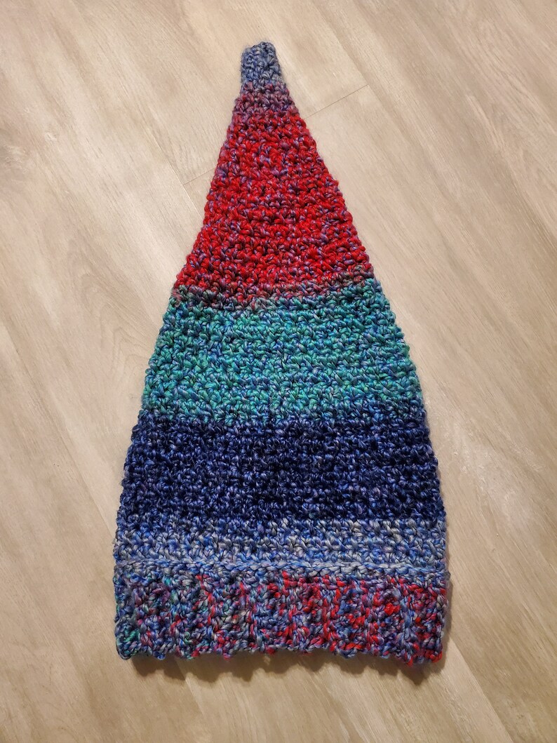 Op de afbeelding: Een driehoekige gehaakte muts met strepen van rood, turquoise, blauw en paars garen.