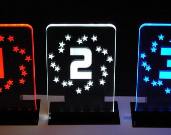 May include: Three acrylic plaques with a circle of stars around a number. The first plaque is red with the number 1, the second is white with the number 2, and the third is blue with the number 3.