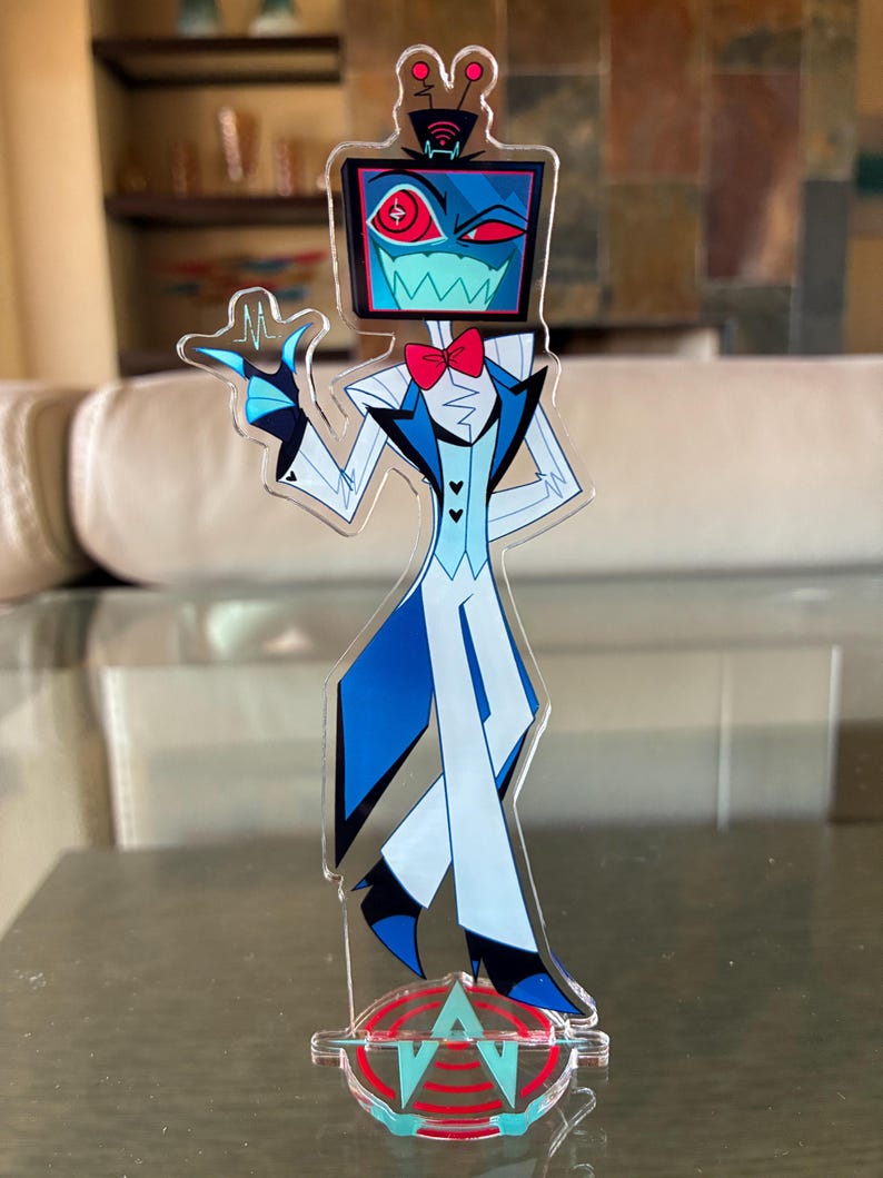 Puede incluir: Una figura de acr&iacute;lico transparente de un personaje de dibujos animados con una cabeza de pantalla de televisi&oacute;n, que lleva un traje azul y blanco con una pajarita roja. La figura est&aacute; de pie sobre una base con las letras "A" y "V" en un dise&ntilde;o rojo y azul. La pantalla muestra un ojo rojo y una boca dentada.