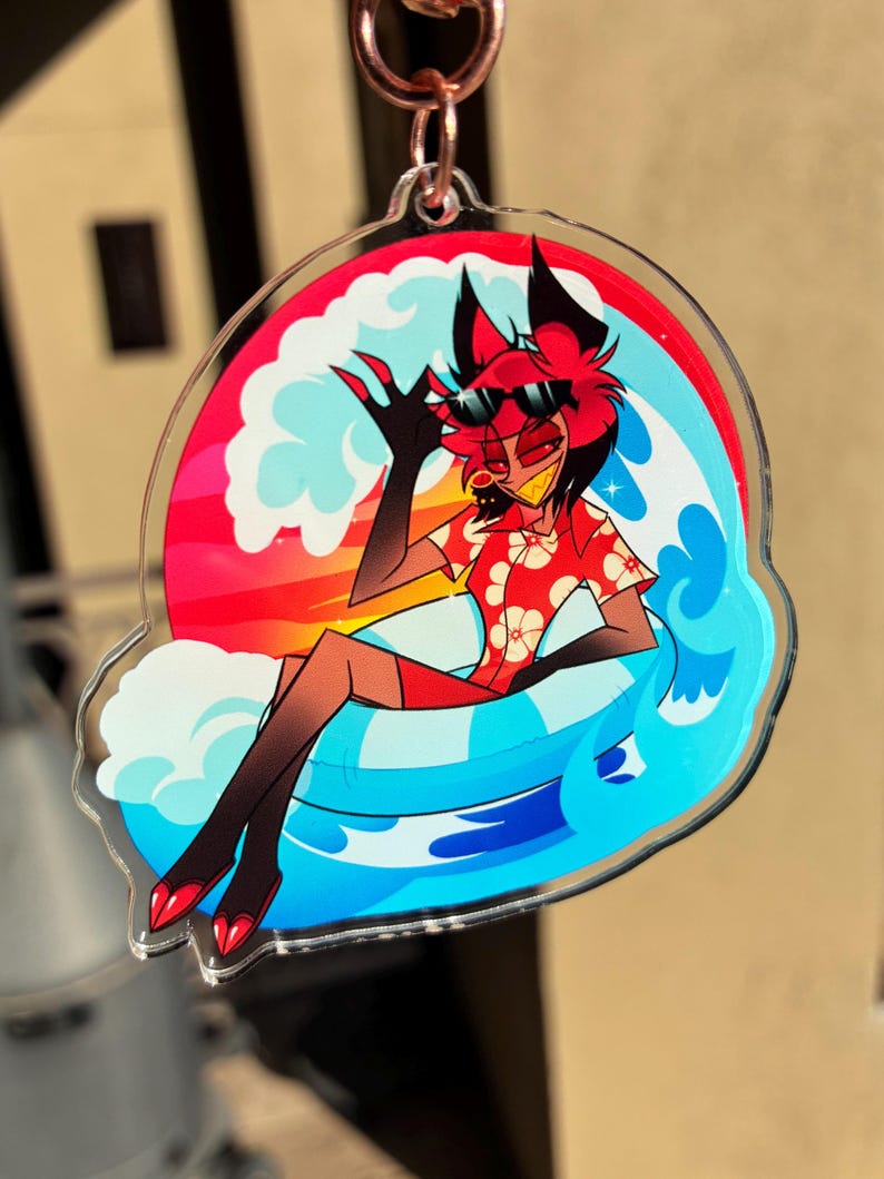 May include: A clear acrylic keychain featuring a cartoon character with red hair and black ears wearing black sunglasses and a red floral shirt. The character sits in a blue and white striped inner tube surrounded by stylized blue waves and a sunset.
