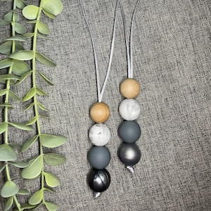May include: Two grey silicone and wood bead necklaces with silver clasps. The beads are in a pattern of grey, white, and brown.