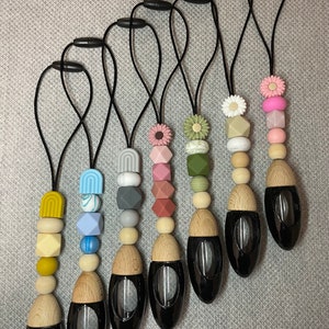 May include: Seven black car air fresheners with wooden caps and colourful silicone beads. Each air freshener has a different pattern of beads, including flowers, geometric shapes, and abstract designs.
