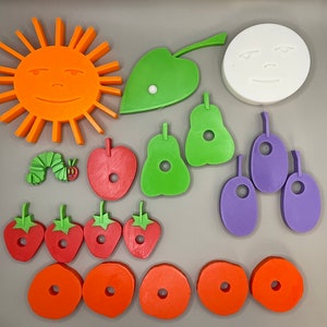 May include: A set of colorful felt pieces shaped like a sun, a caterpillar, a leaf, pears, strawberries, and other fruits. The pieces are designed to be used for a craft project or to create a story.
