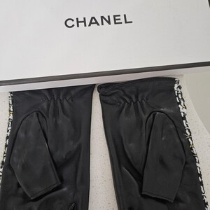 May include: Black leather fingerless gloves with white and black trim, and a white box with the word "CHANEL" printed in black. The gloves have a classic design.