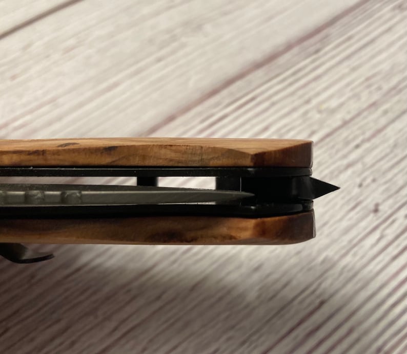 May include: Close-up of a wooden handled pocket knife with a black blade. The blade is partially open and the tip is visible.