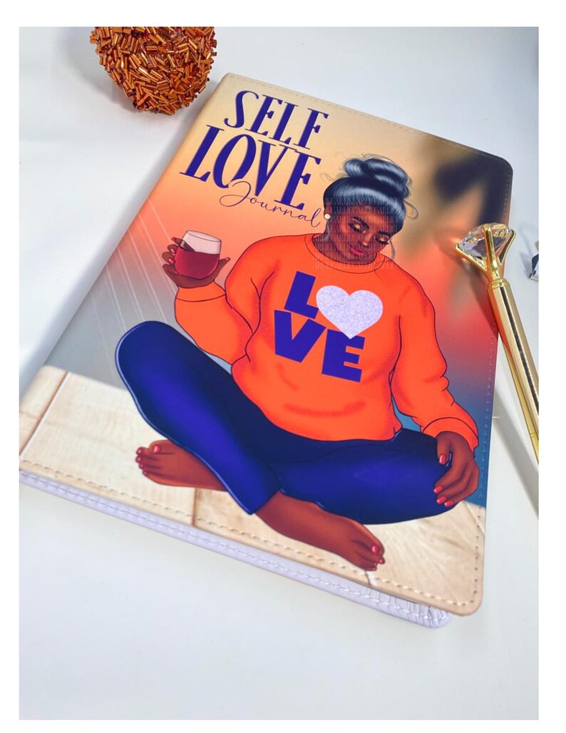 Pu&ograve; includere: Diario di Autoamore con un'illustrazione colorata di una donna seduta con un bicchiere di vino. La donna indossa una camicia arancione con le parole "Love" in lettere viola e un cuore bianco sul davanti. La copertina del diario ha uno sfondo bianco con un motivo a venature di legno marrone chiaro.