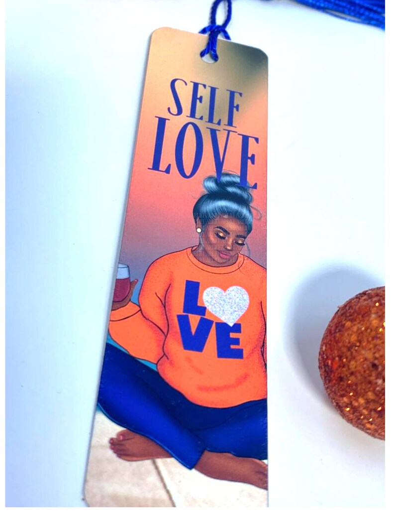 Pu&ograve; includere: Un segnalibro con una donna con un bicchiere di vino, che indossa una felpa arancione brillante con la parola "LOVE" in lettere blu e un cuore bianco. Lo sfondo &egrave; un tramonto con le parole "SELF LOVE" in lettere blu in alto.