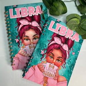 Pode incluir: Dois cadernos espiralados com a palavra "LIBRA" em rosa. As capas apresentam uma mulher com cabelo rosa e um laço rosa, segurando uma caneca com "BIG LIBRA ENERGY". O fundo é turquesa com estrelas rosas.
