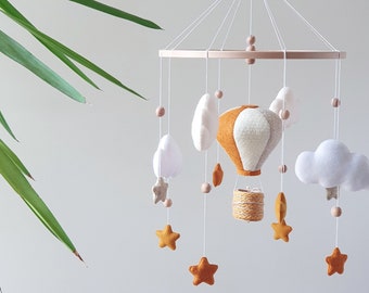 May include: A white and orange felt hot air balloon mobile with white clouds, stars, and wooden beads hanging from a wooden ring.