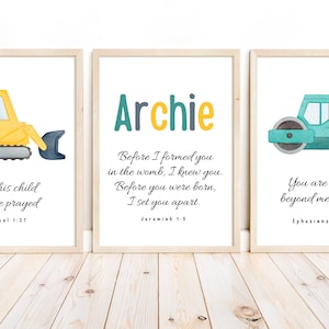 May include: Three framed prints with watercolour illustrations of construction vehicles. The first print features a yellow excavator with the text "For this child I have prayed 1 Samuel 1:27". The second print features a blue and yellow text that reads "Archie" and the text "Before I formed you in the womb, I knew you. Before you were born, I set you apart. Jeremiah 1:5". The third print features a blue steamroller with the text "You are loved beyond measure. Ephesians 3:19".