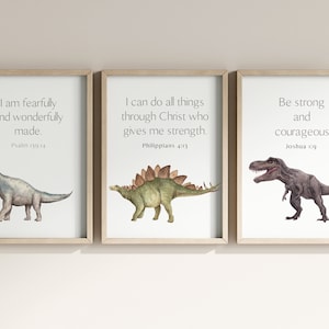 May include: Three framed prints with watercolor illustrations of dinosaurs and inspirational quotes. The first print features a Brachiosaurus with the quote "I am fearfully and wonderfully made." from Psalm 139:14. The second print features a Stegosaurus with the quote "I can do all things through Christ who gives me strength." from Philippians 4:13. The third print features a Tyrannosaurus Rex with the quote "Be strong and courageous." from Joshua 1:9.