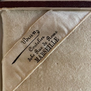 May include: A white satin ribbon with black text that reads "Brums Coutelier 30 bis Rue de Rome MARSEILLE".
