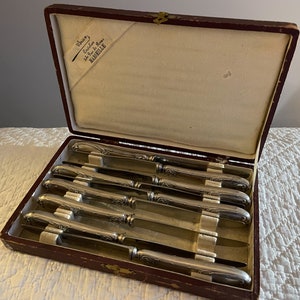 Peut inclure: Un coffret en velours rouge contenant huit couteaux à beurre en argent plaqué. Le coffret porte une étiquette indiquant "Chervin, Coutellerie Fine, Marseille".