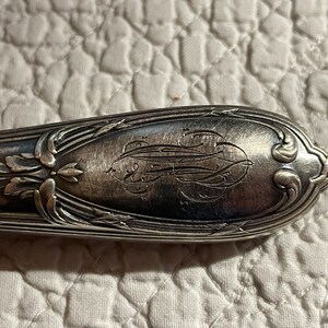 May include: Close-up of a silver handle with an ornate design and an engraved monogram.