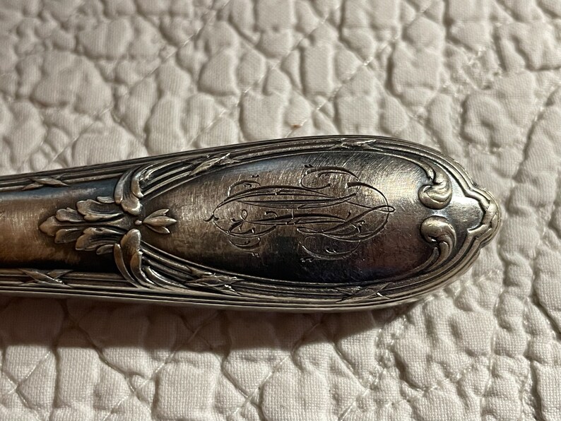 May include: Close-up of a silver handle with an ornate design and an engraved monogram.