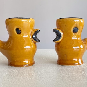 Puede incluir: Dos hueveras de cerámica con forma de pato. Las hueveras están esmaltadas en un amarillo mostaza brillante con detalles negros para los ojos y los picos. Las hueveras de pato tienen un diseño único y caprichoso.
