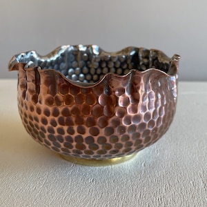 May include: A hammered copper bowl with a scalloped rim and a brass base. The bowl has a textured, hammered surface.