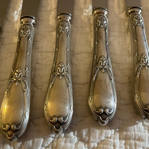 May include: Set of six silver-plated dinner knives with ornate handles. The handles have a detailed floral design and a polished finish.