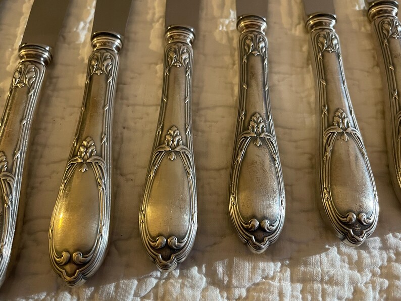 May include: Set of six silver-plated dinner knives with ornate handles. The handles have a detailed floral design and a polished finish.