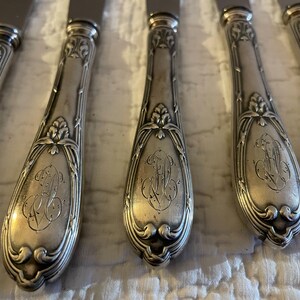 May include: Set of six silver-plated dinner knives with ornate handles. Each handle features a floral design and an engraved monogram.