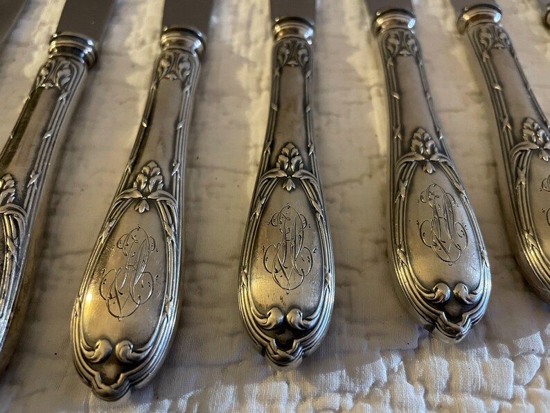 May include: Set of six silver-plated dinner knives with ornate handles. Each handle features a floral design and an engraved monogram.