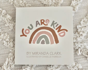 May include: A square, off-white children's book with the words "YOU ARE KIND" above a rainbow illustration in shades of brown, pink, and gray. The book's cover also includes the author's name, Miranda Clark, and the illustrator's name, Danielle Fabrega.