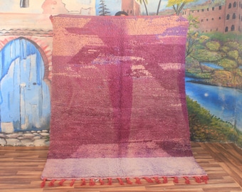 May include: A large, rectangular rug with a textured surface. The rug features a gradient of pink and purple hues, with a lighter border and fringe. The design includes a central, vertical pattern. The rug is likely made of wool or a similar material.