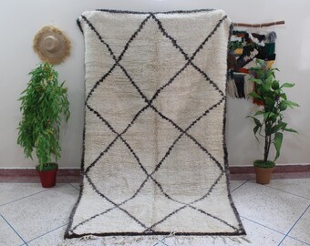 May include: A rectangular off-white area rug featuring a dark brown diamond grid pattern. The rug has a thick, shaggy pile texture and includes a fringe detail along the bottom edge, creating a distinct geometric design across the surface.