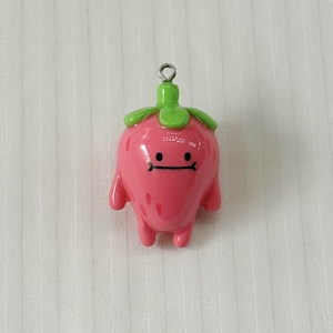 May include: A glossy pink strawberry-shaped charm with a smooth finish, featuring a green stem top, two small arms, two legs, and a simple black line face with two dots for eyes. A small silver metal jump ring is attached to the top stem.