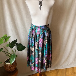 May include: A midi-length skirt featuring a vibrant floral pattern in shades of magenta, teal, and blue set against a black background with intricate gold-toned filigree details. The skirt has a high-waisted fit with soft pleats and a flared silhouette.