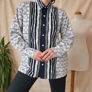 May include: A button-down shirt with a unique design. The shirt features a combination of checkered and striped patterns in shades of gray, white, and navy blue. The center panel has vertical stripes, while the sleeves and sides have a checkered pattern.