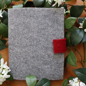 May include: A grey felt notebook with a red felt bookmark. The notebook is surrounded by white flowers and green leaves.