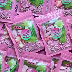 May include: Several pink cellophane bags filled with assorted candies, including pink sprinkles, green gummy sticks, and flower-shaped sweets. Each bag has a circular sticker that reads "Thank You For Coming Along" with a witch hat and broom design.