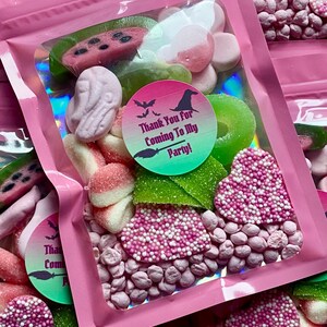 May include: Pink cellophane bags filled with Halloween-themed candies. The bags contain a variety of sweets, including watermelon slices, gummy rings, and heart-shaped candies covered in sprinkles. The bags have a sticker that says "Thank You For Coming To My Party!"