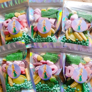 May include: Six clear plastic bags filled with colourful candy, each bag has a sticker with a cartoon image of Tinkerbell. The bags are on a wooden surface.