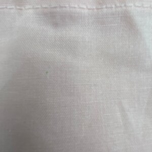 May include: Close-up of a white fabric with a subtle texture. The fabric has a smooth, even surface with a slight sheen.