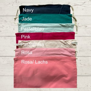 May include: A set of seven drawstring bags in various colors, including navy, jade, light blue, pink, cream, light pink, and coral. The bags are lined up vertically, with the color names written in white text on each bag.