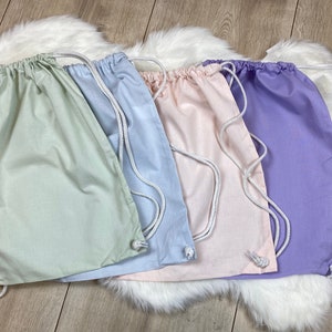 May include: Four drawstring bags in different pastel colors: light green, light blue, light pink, and lavender. The bags are made of a soft, cotton fabric and have white drawstrings.