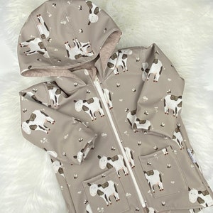 May include: A gray hooded jacket with a zipper closure and two pockets. The jacket has a cow print pattern with white and black spots.