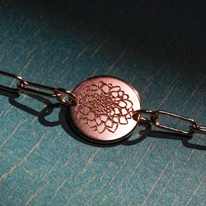 Puede incluir: Un brazalete de cadena dorada con un colgante redondo que presenta un diseño floral detallado.