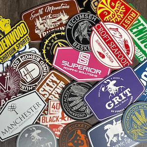 May include: A collection of various stickers with different designs and text. The stickers feature logos, text, and illustrations, including a mountain scene, a Native American profile, and the words "CROFT SEAFOOD".