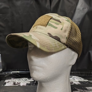 May include: A camouflage baseball cap with a brown mesh back panel and a tan velcro patch on the front.
