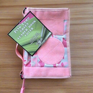 Pu&ograve; includere: Copertina per libro leader rosa mimetico con una toppa circolare rosa e un'etichetta che recita "Pink Camo Green Leader Book Cover". La copertina ha un cinturino rosa e un motivo mimetico rosa e bianco.