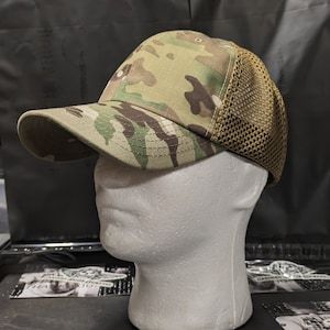 May include: A camouflage baseball cap with a curved brim and a mesh back. The cap features a pattern of green, brown, and tan colors. The mesh back is a tan color.