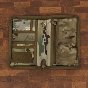 Pu&ograve; includere: Organizer piatto aperto con motivo mimetico e pi&ugrave; scomparti. Include tasche trasparenti, una tasca con cerniera e una tasca a rete. L'organizer &egrave; realizzato in tessuto resistente e ha una chiusura con cerniera. La combinazione di colori include sfumature di verde, marrone e beige.